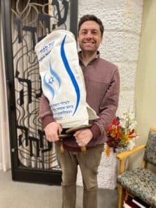 Hazzan Fradkin carries one of the Torahs with the cover from the Simchat Torah project